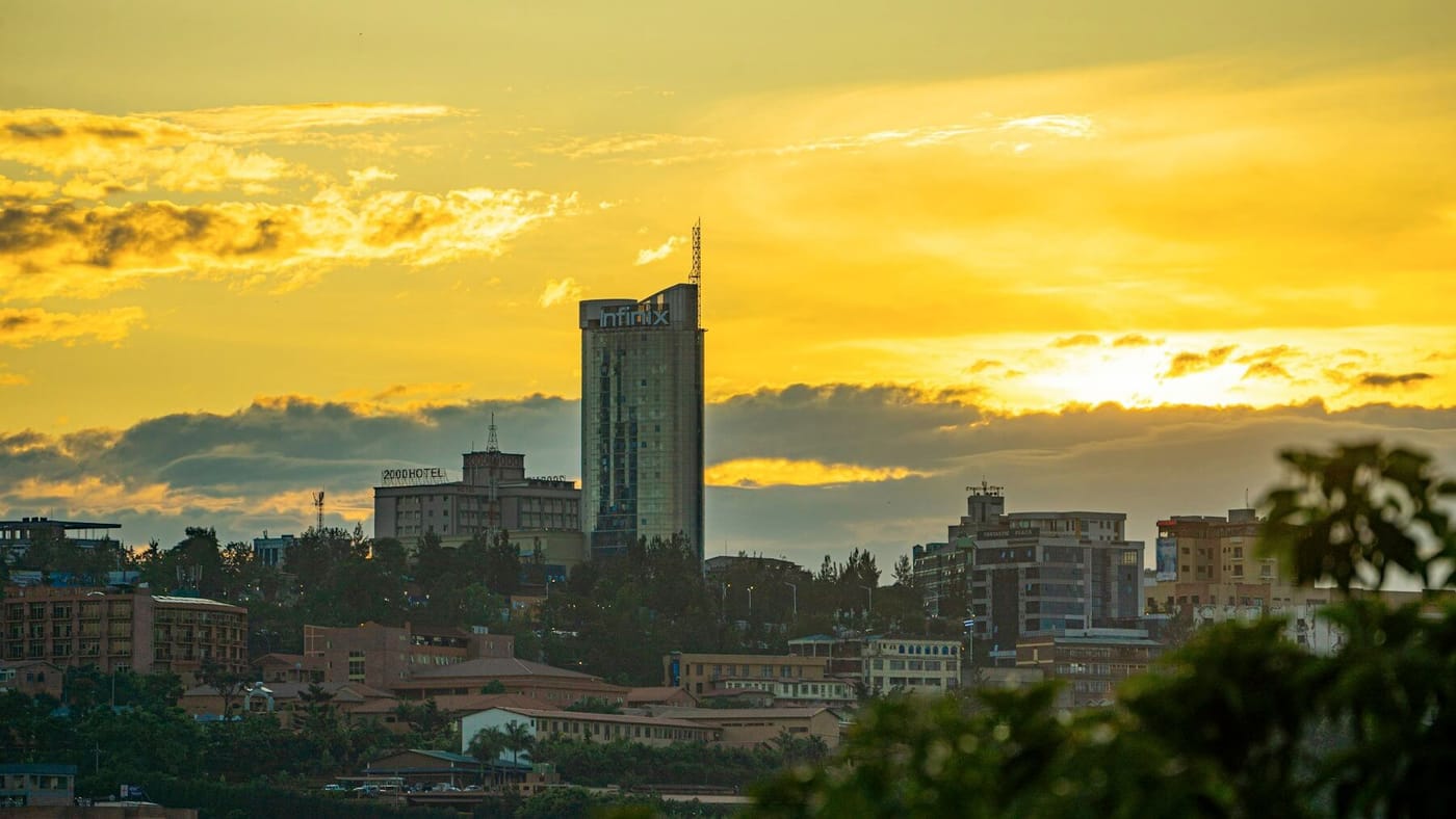 The Kigali skyline at sunset, with a tall glass tower rising above the city's hills